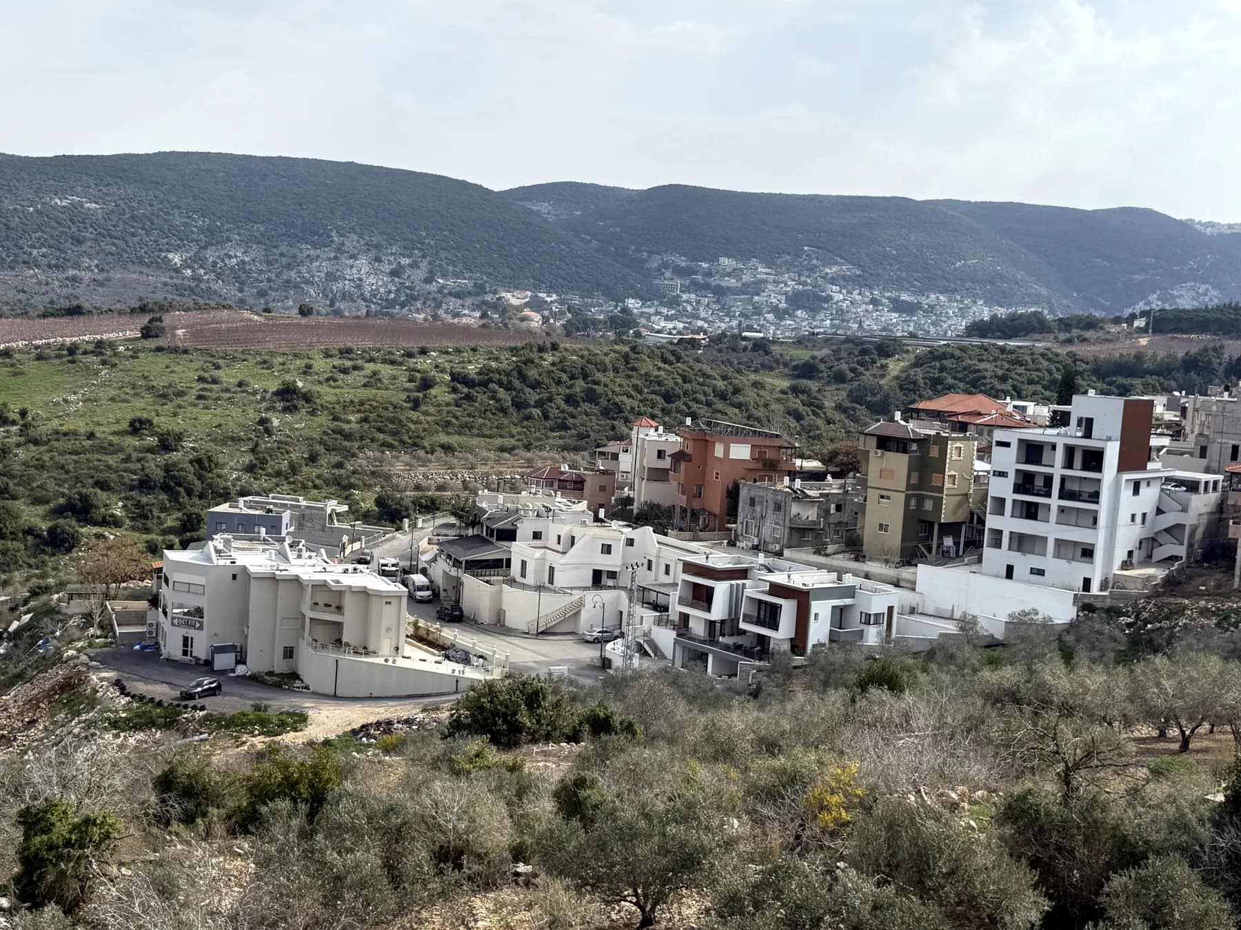 A neighbourhood of new white houses in Kisra-Sumei, with green hills and a mountain village behind.