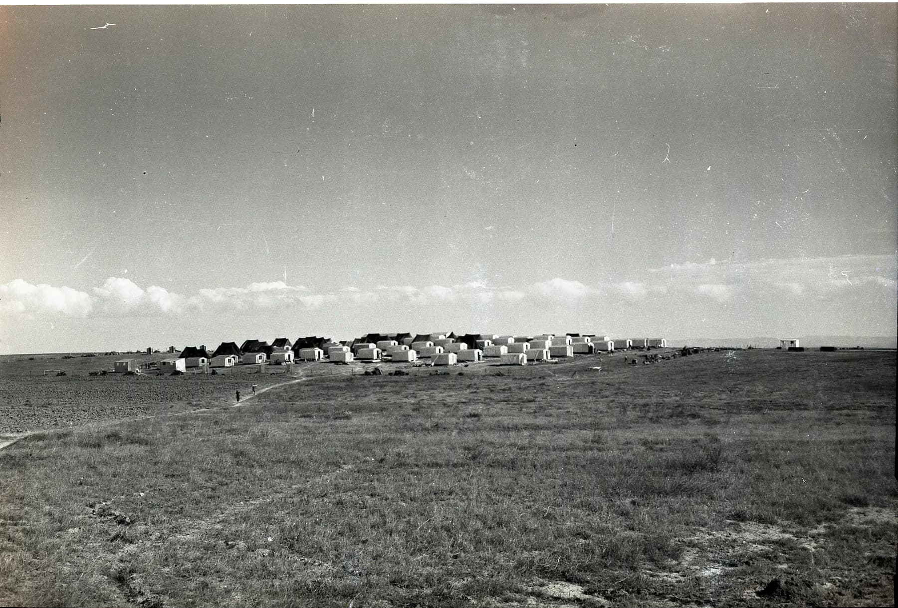 An old black-and-white photograph of rows of small huts standing on an open plain at Kokhav Michael, under a wide sky.