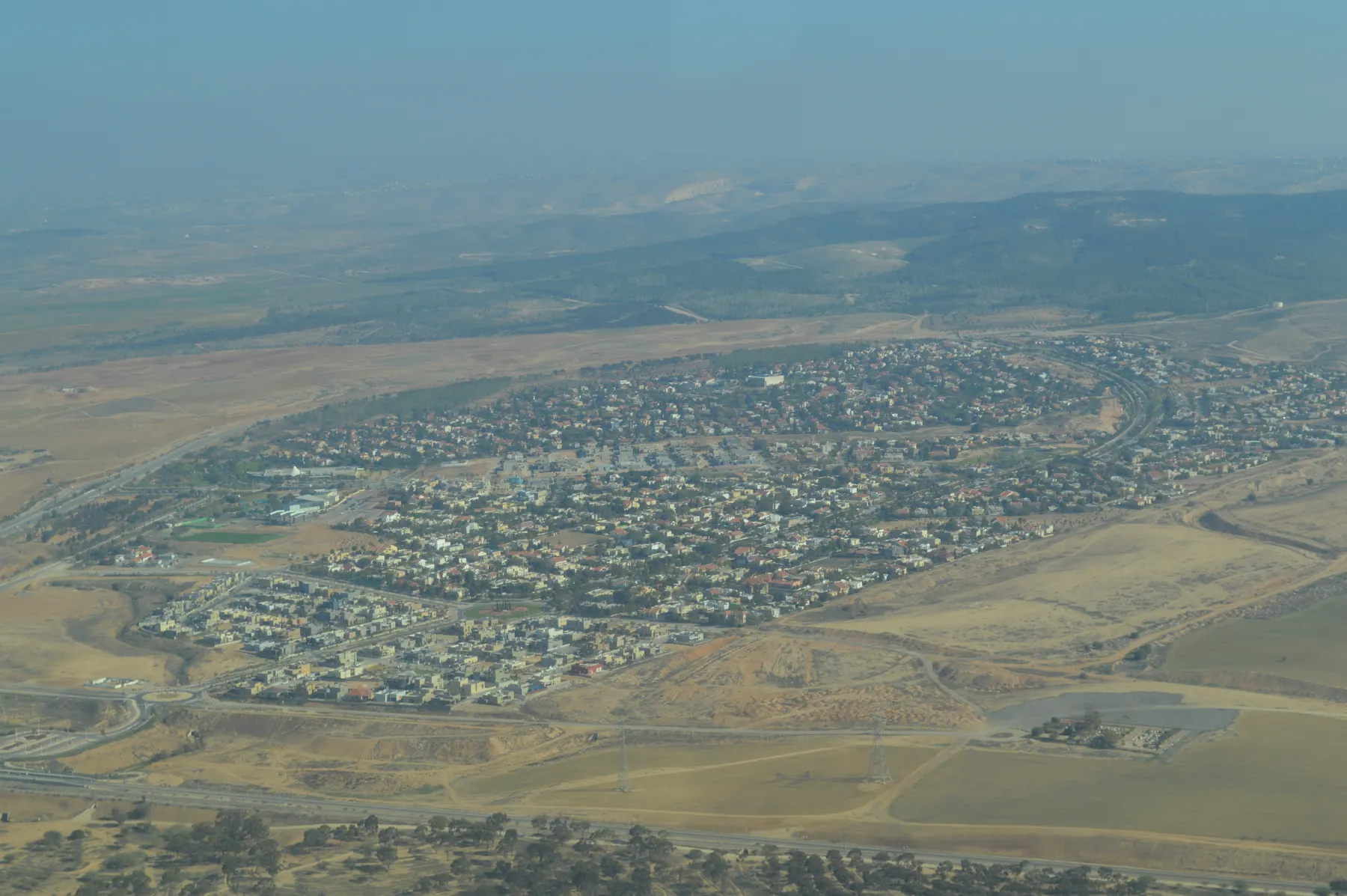 An aerial view of Lehavim, its houses packed into a rounded layout among dry fields, with roads curving around it.
