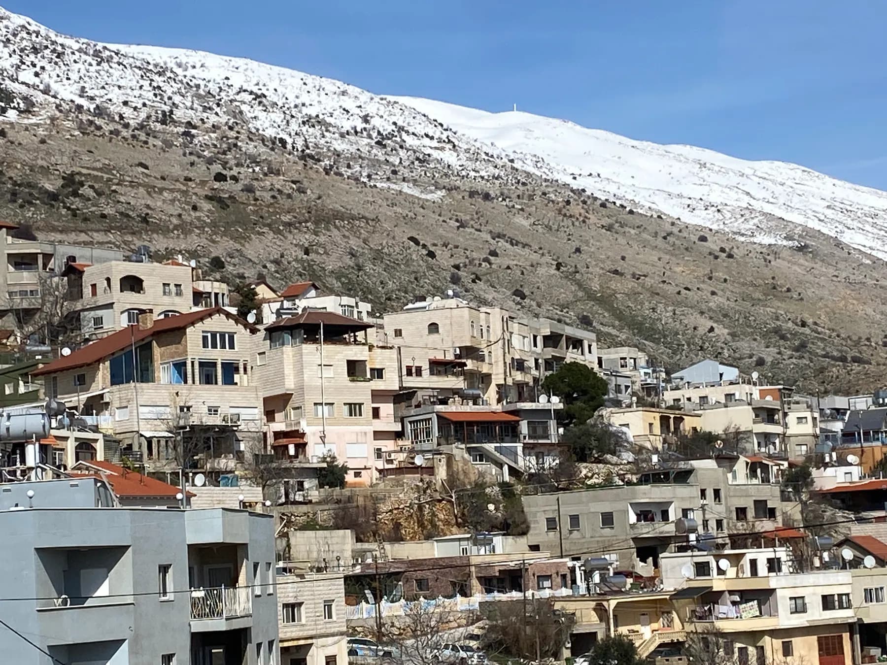 Stone houses of Majdal Shams climbing the slope, with the snow-covered Hermon above.