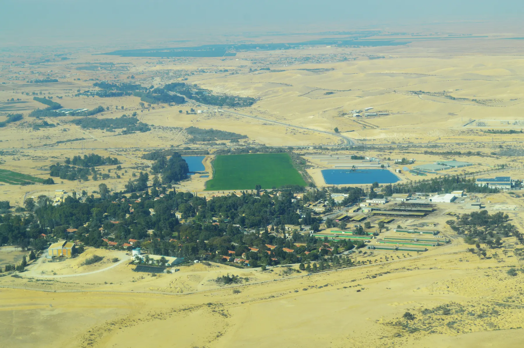 An aerial view of Mashabei Sadeh, with its houses among dense trees and green fields and blue reservoirs in the surrounding desert.