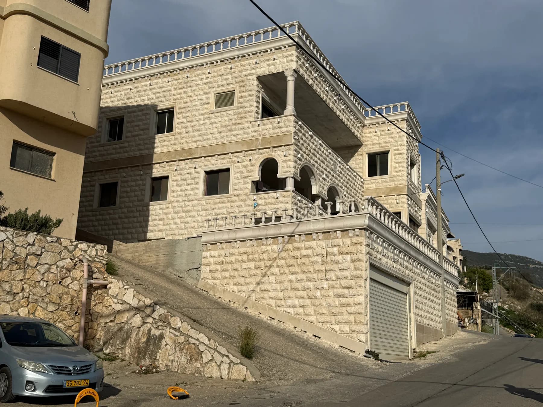 A large stone house on a sloping street in Nahef, under a blue sky.