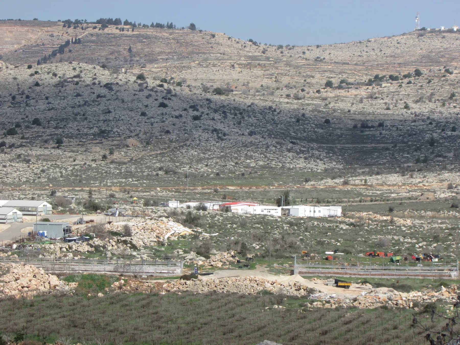 שורות של בתים טרומיים לבנים בשכונה בעפרה, למרגלות מדרון סלעי עם שיחים.