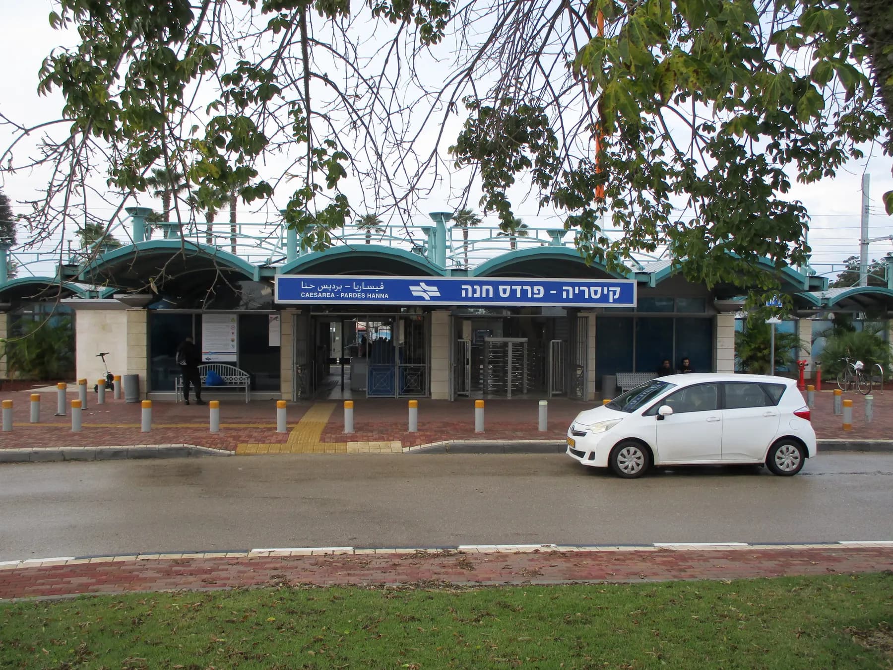 The entrance building of Caesarea-Pardes Hanna railway station, with its name sign in Hebrew, Arabic and English and a car parked in front
