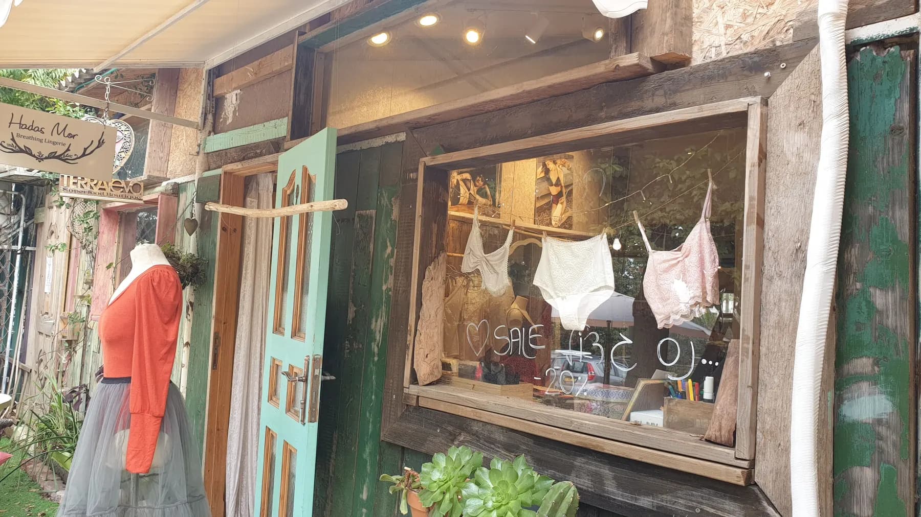 A second-hand shop front in Pardes Hanna: a turquoise wooden door, a dressed mannequin and a window with lingerie hung on a line and a hand-written sale sign