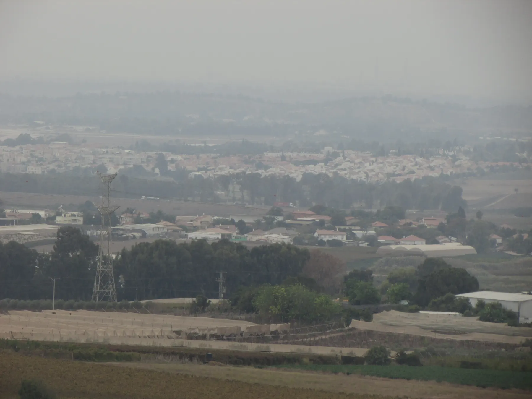 בתים בעלי גגות אדומים בפדיה, מעבר לשדות מכוסים ברשתות ועמוד חשמל, ומאחוריהם עיירה גדולה יותר באובך.