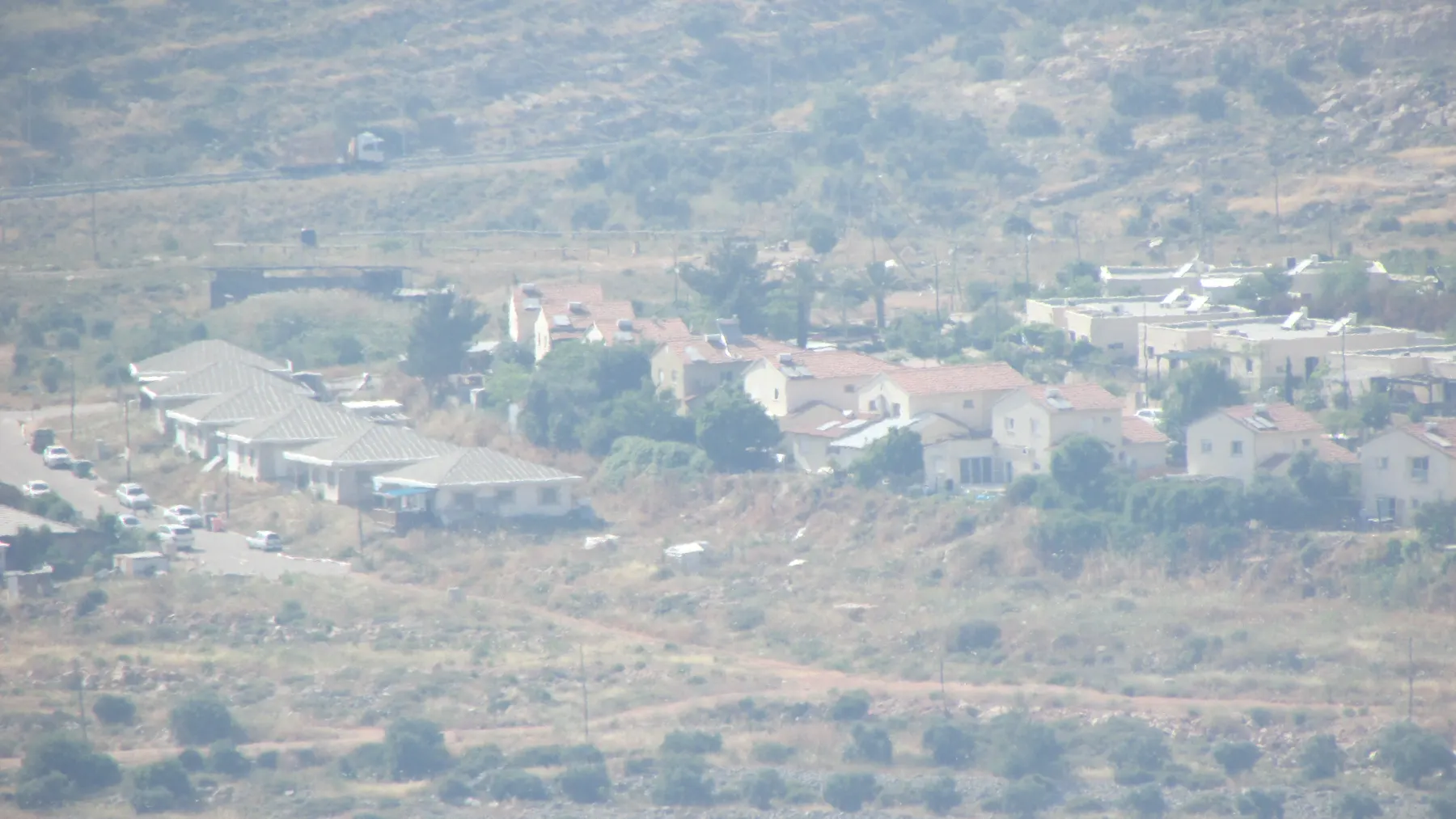 בתים עם גגות רעפים אדומים ושורת בתים עם גגות אפורים על מדרון ברחלים, במבט על פני מדרונות בתה ביום אביך.