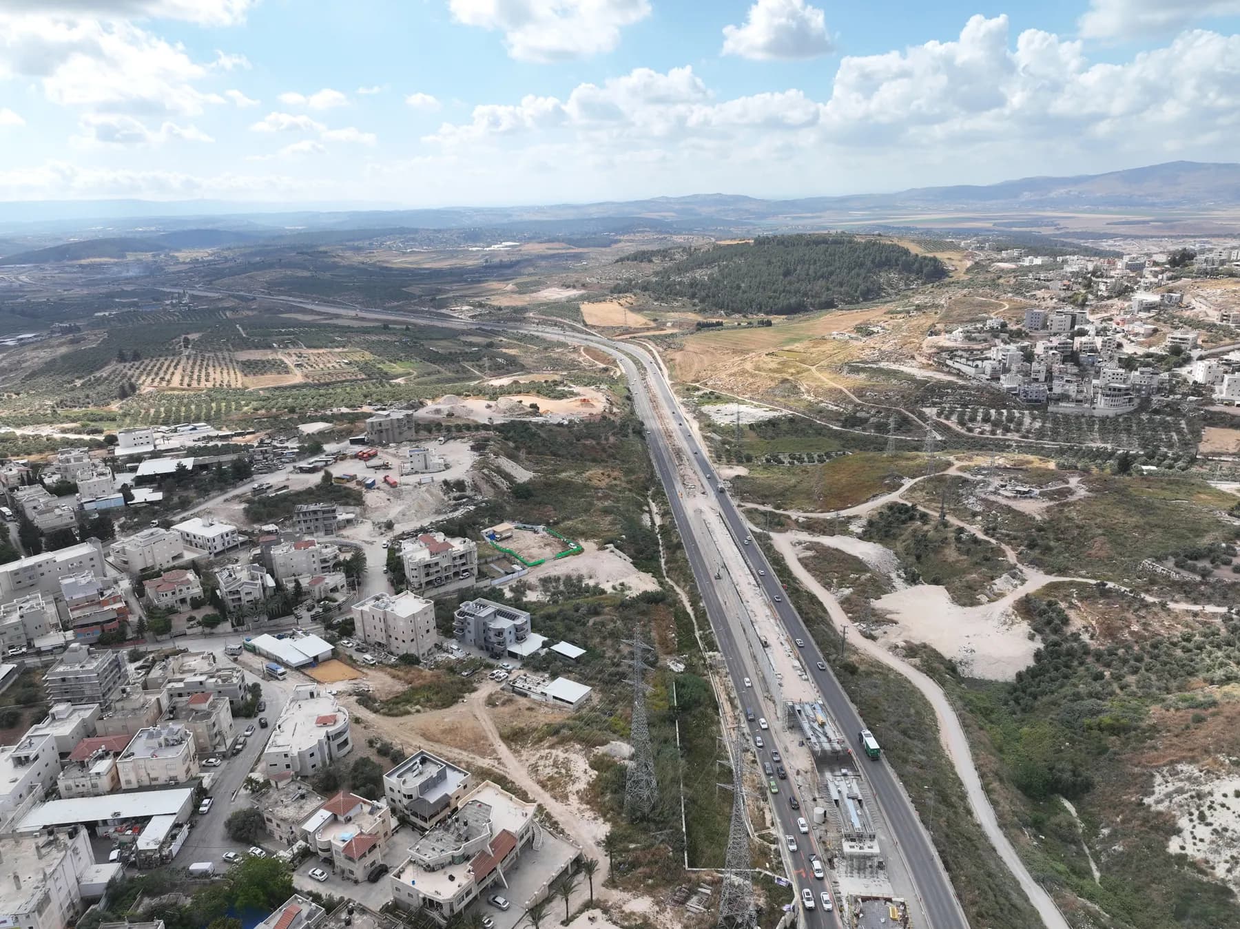 An aerial view of houses in Reineh beside a highway, with olive groves and hills beyond.
