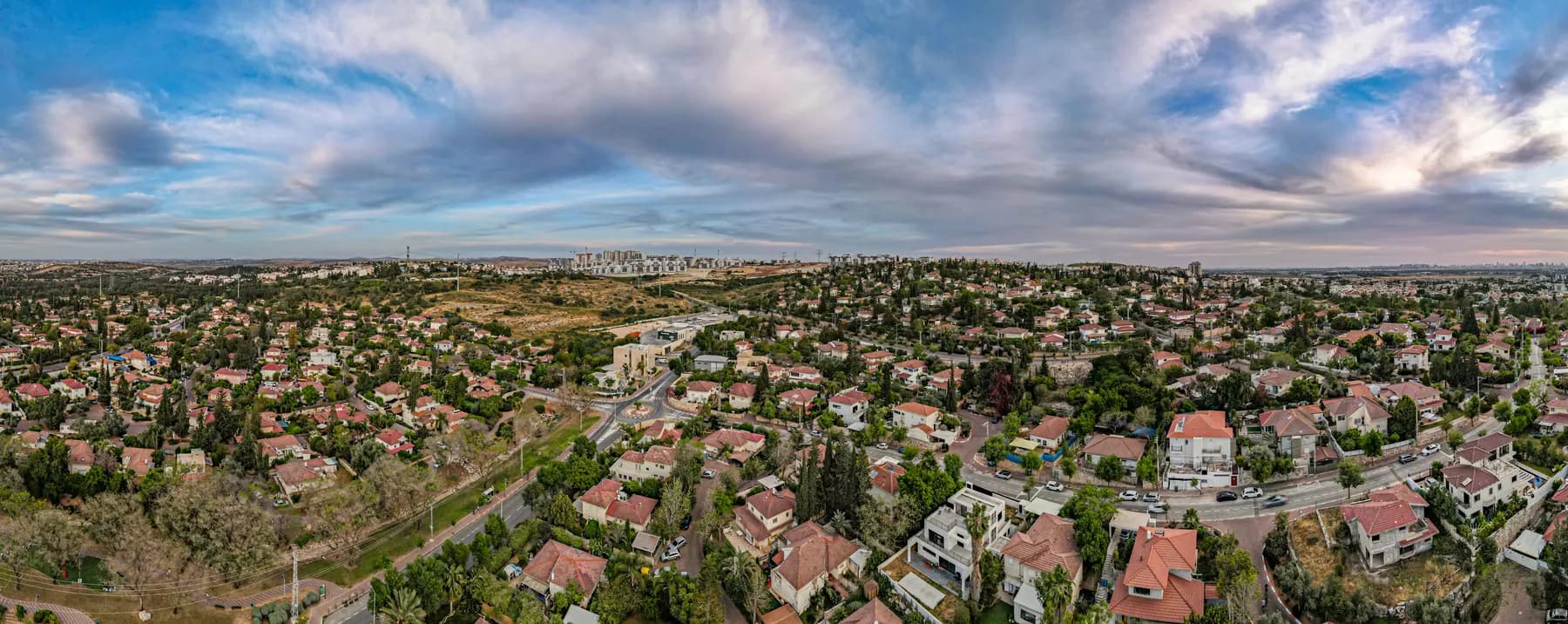A wide aerial view over the Givat Tal neighbourhood of Rosh HaAyin, with red-roofed houses, streets and towers on the horizon.