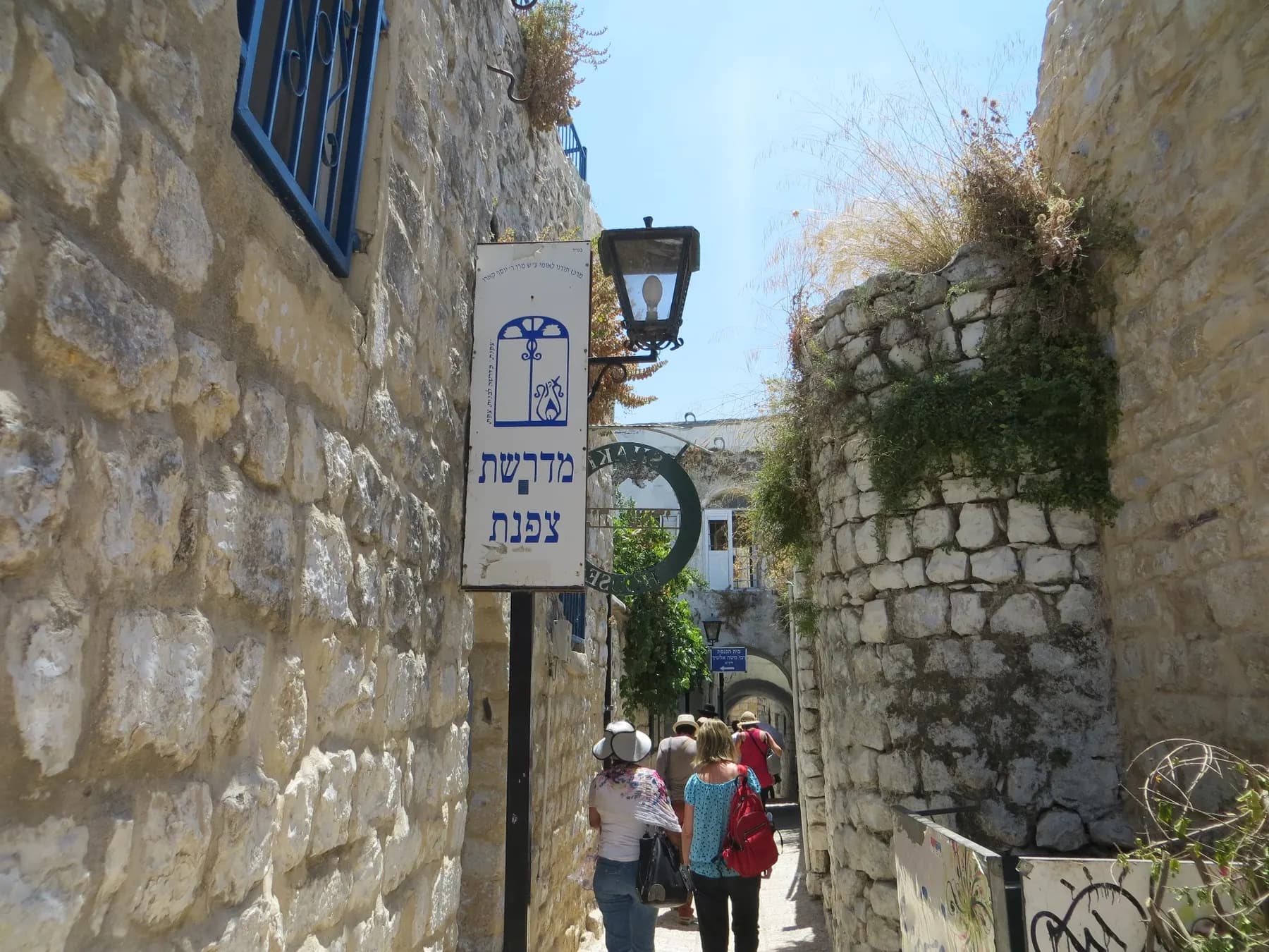 A stone lane in Safed's Old City, with visitors walking between old walls under a street lamp.