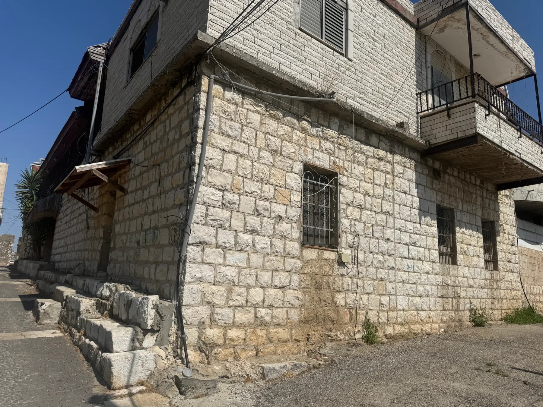An old house of squared stone blocks with barred windows and a balcony above, on a lane in the old core of Sajur.
