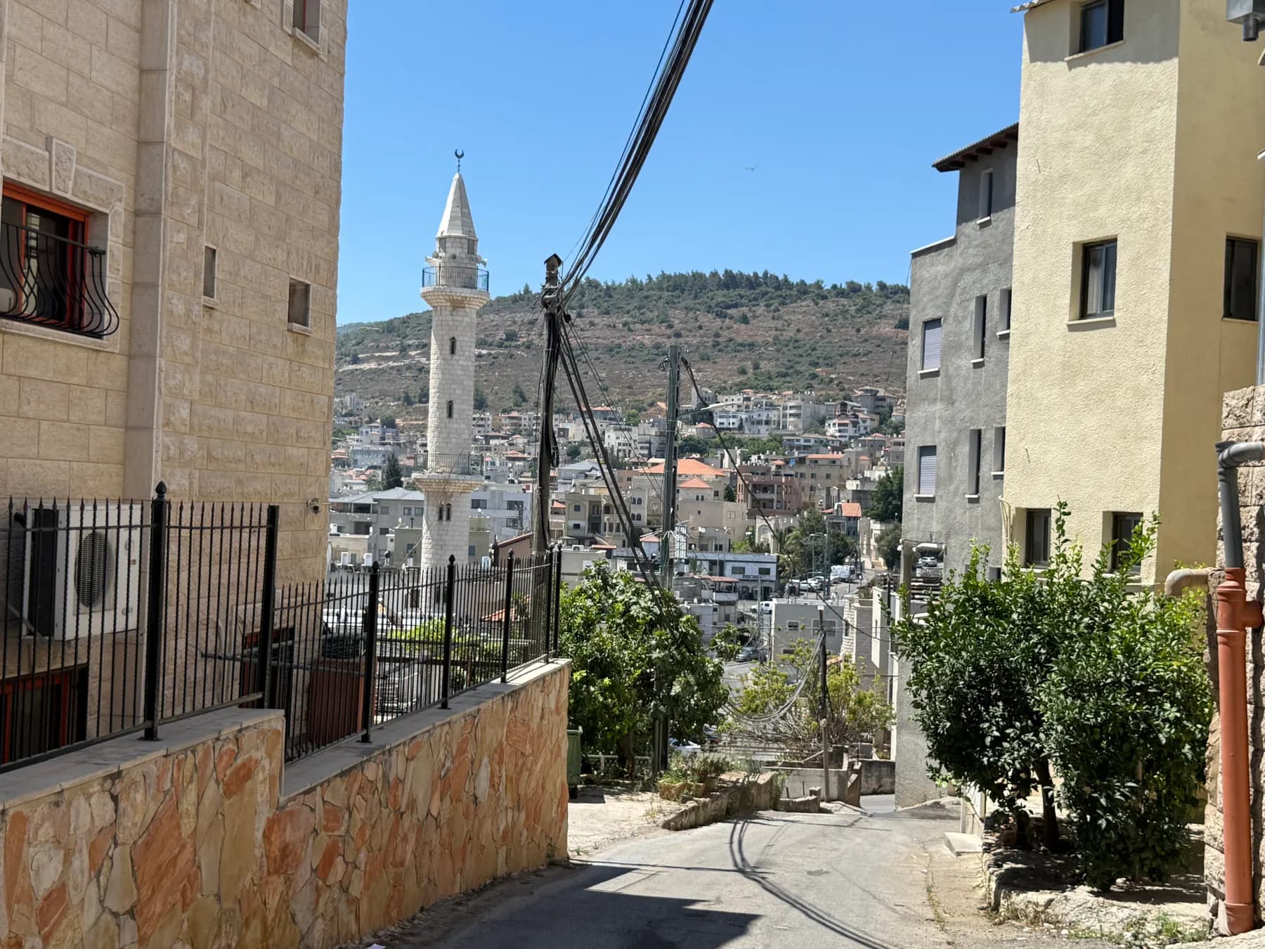 A narrow street in Sakhnin looking toward a white minaret, with houses climbing the hill behind.