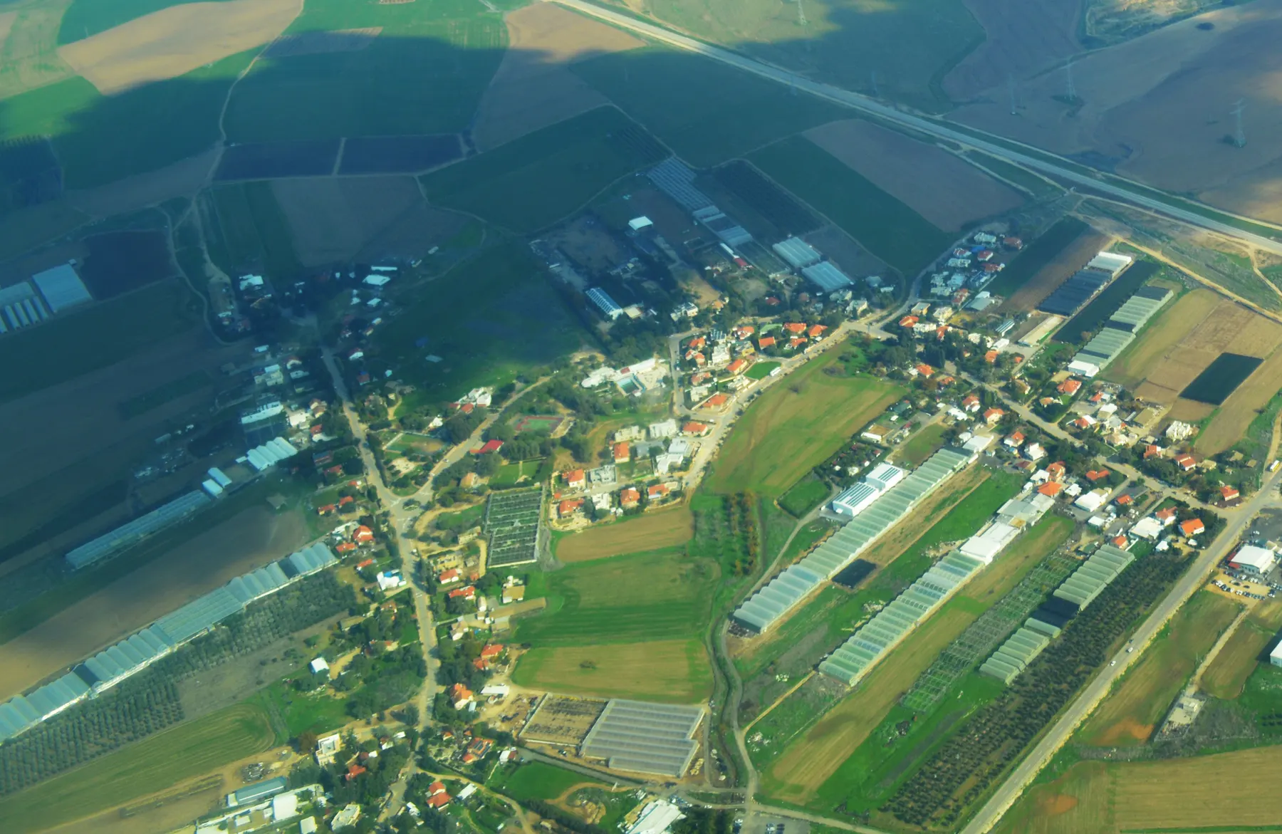 An aerial view of Sgula, with houses and gardens along its roads and greenhouses and fields around them.