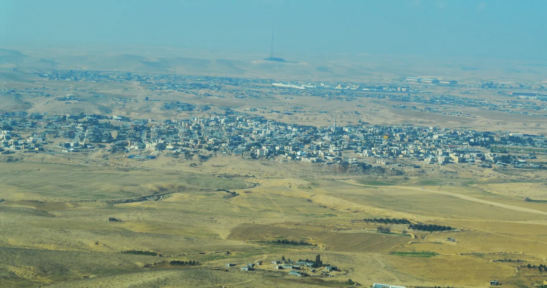 A view over the houses of Shaqib al-Salam (Segev Shalom) spread across the desert, with more built-up land on the horizon.