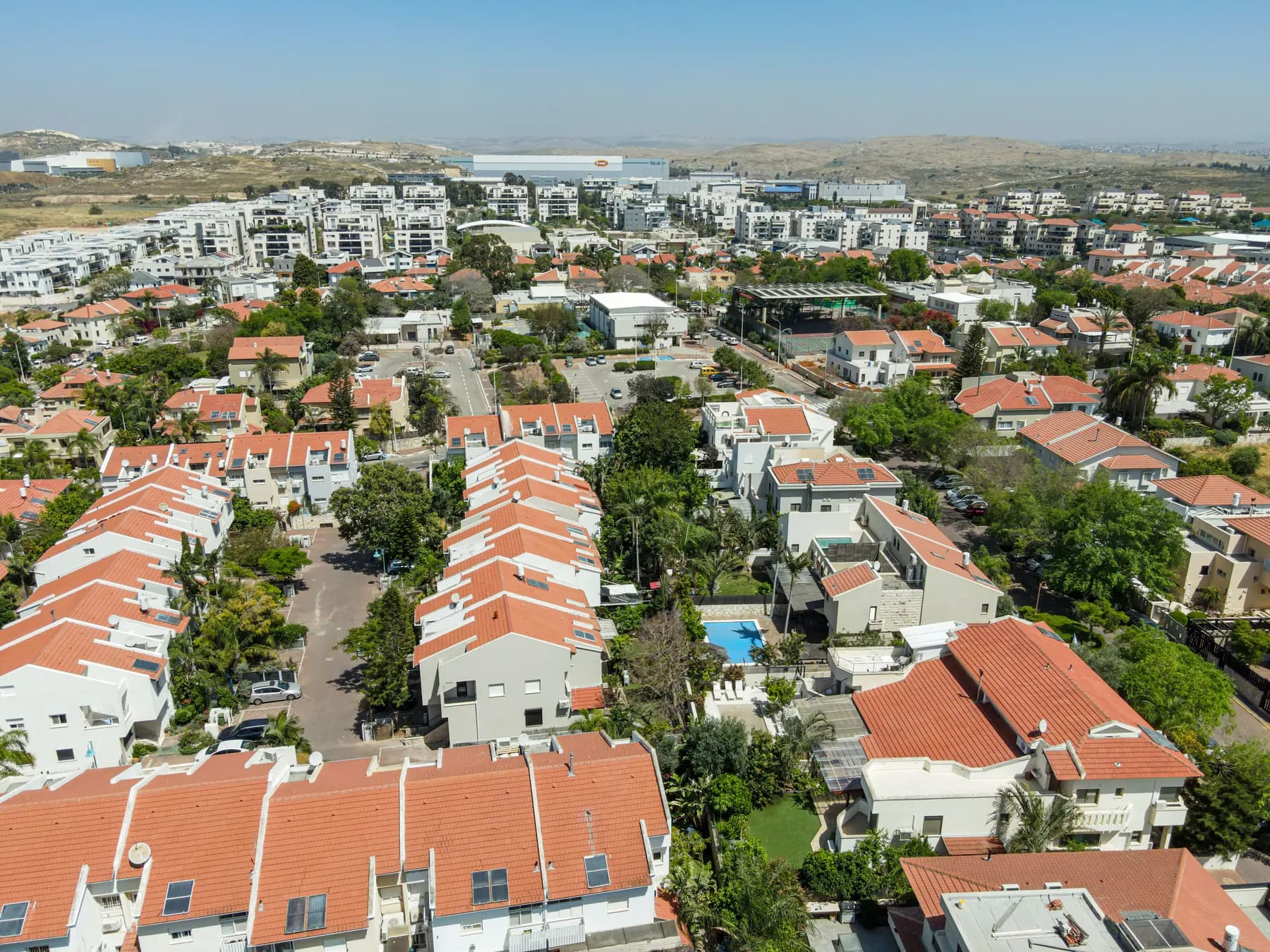 An aerial view of Shoham, with rows of red-roofed houses and gardens and apartment buildings beyond.