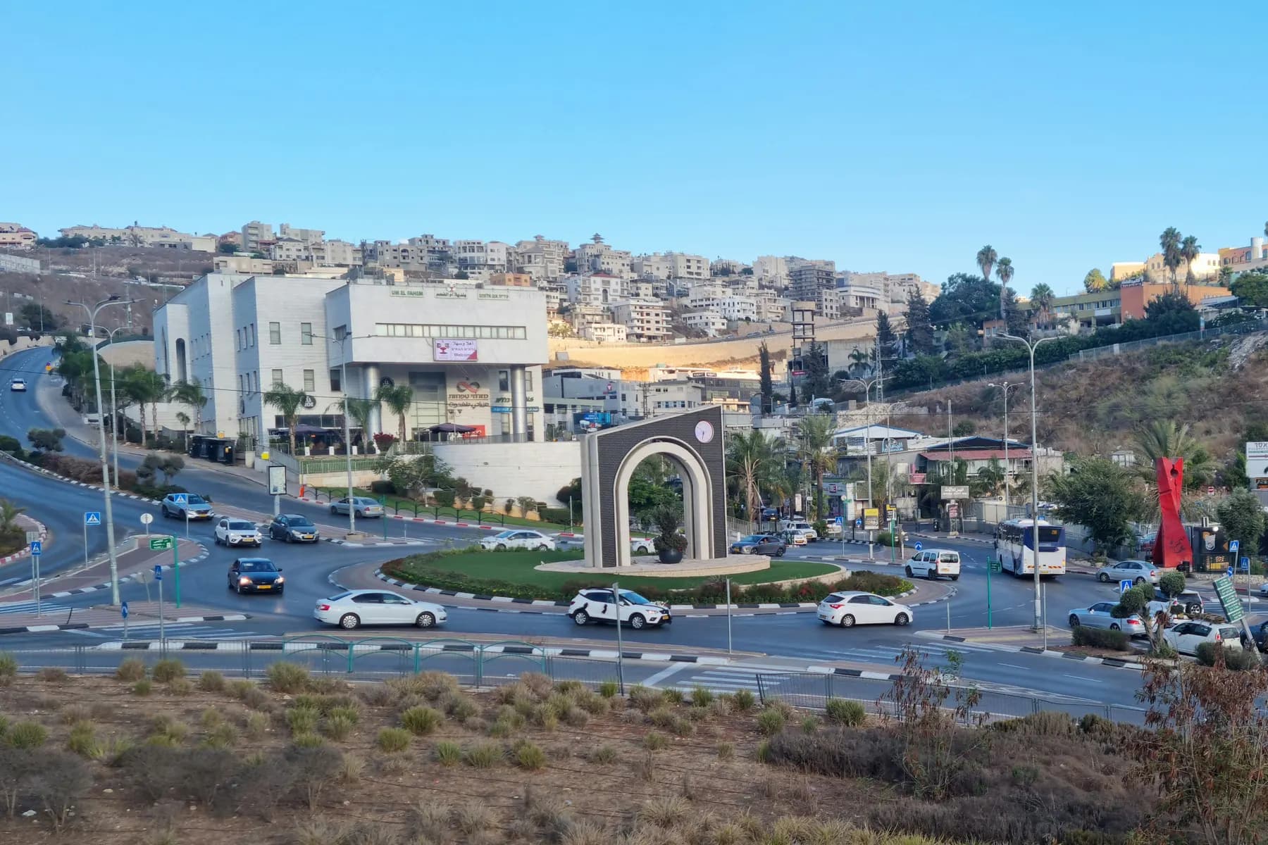 The entrance roundabout of Umm al-Fahm, with a stone arch and clock, and houses climbing the hillside behind.