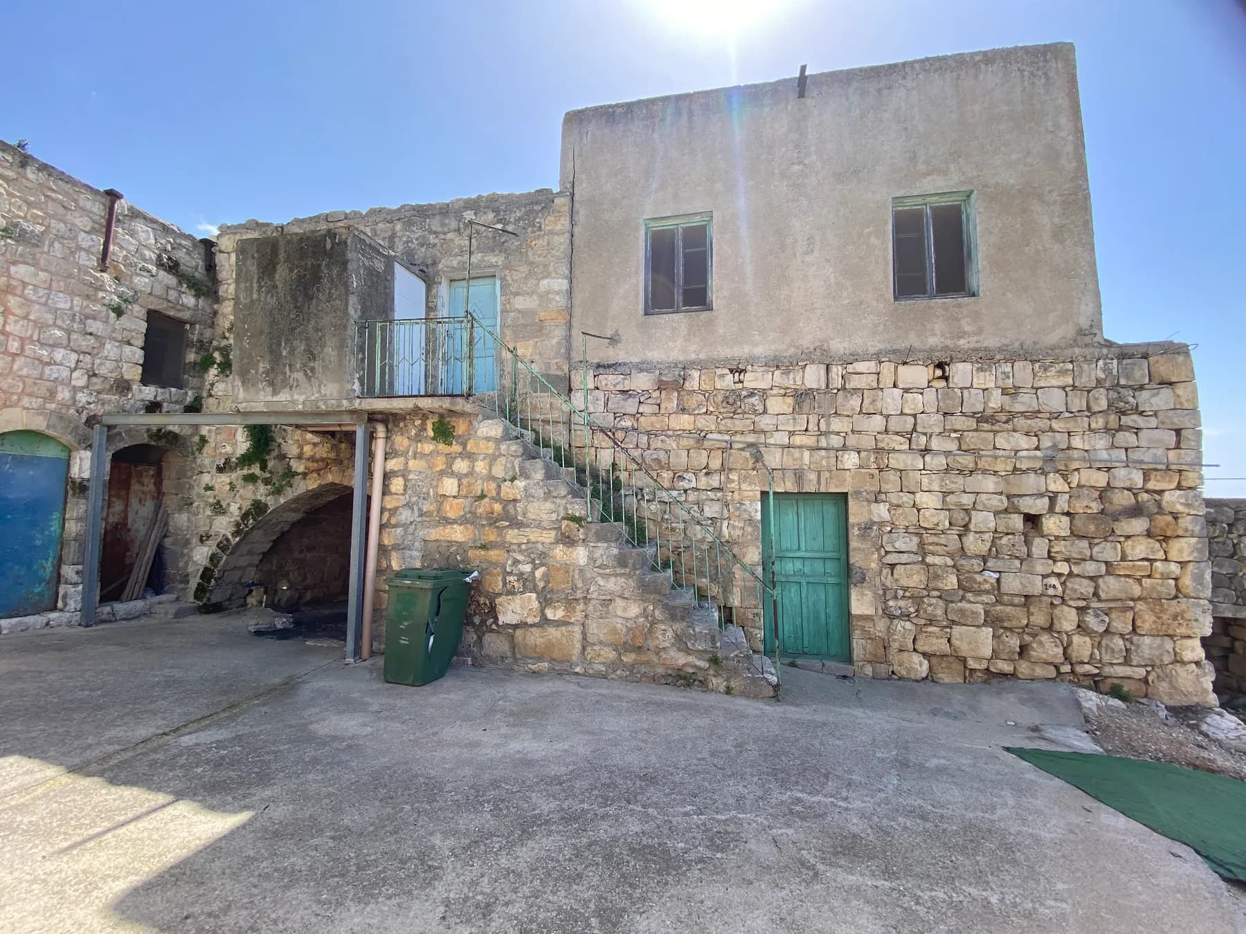 An old stone house with an outside staircase and green doors around an open courtyard in Yanuh-Jat.