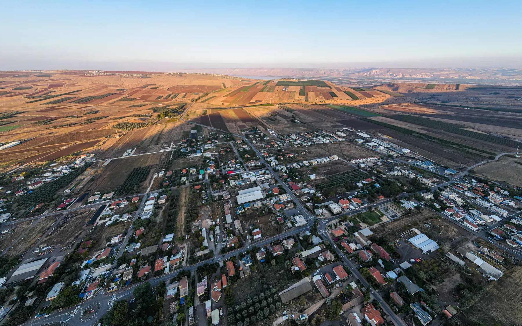 An aerial view of Yavne'el, its houses and roads laid out in a grid, with fields stretching across the valley to the hills on the horizon.