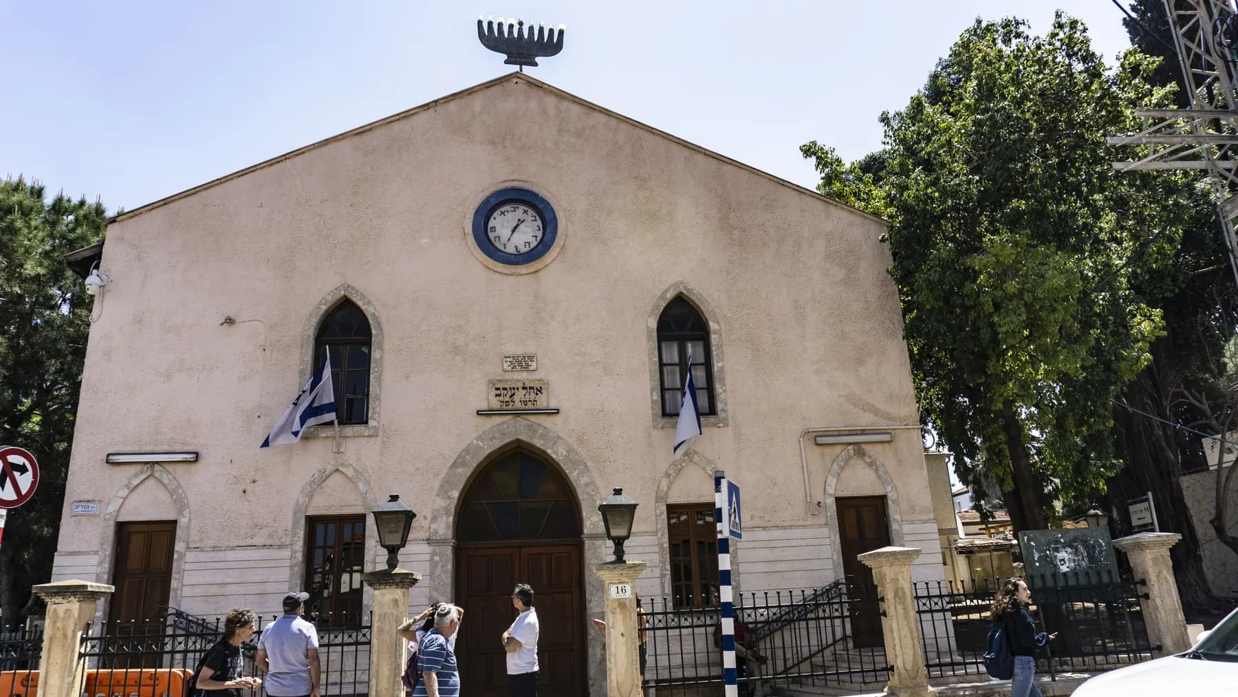 The stone front of the Ohel Yaakov synagogue in Zichron Yaakov, with its clock, arched door and Israeli flags