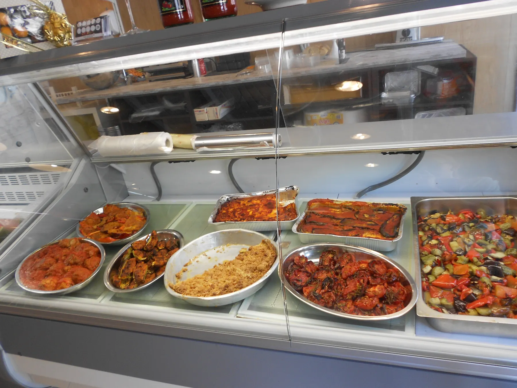 A deli counter with trays of cooked dishes: stuffed peppers, rice, stews and roasted vegetables.