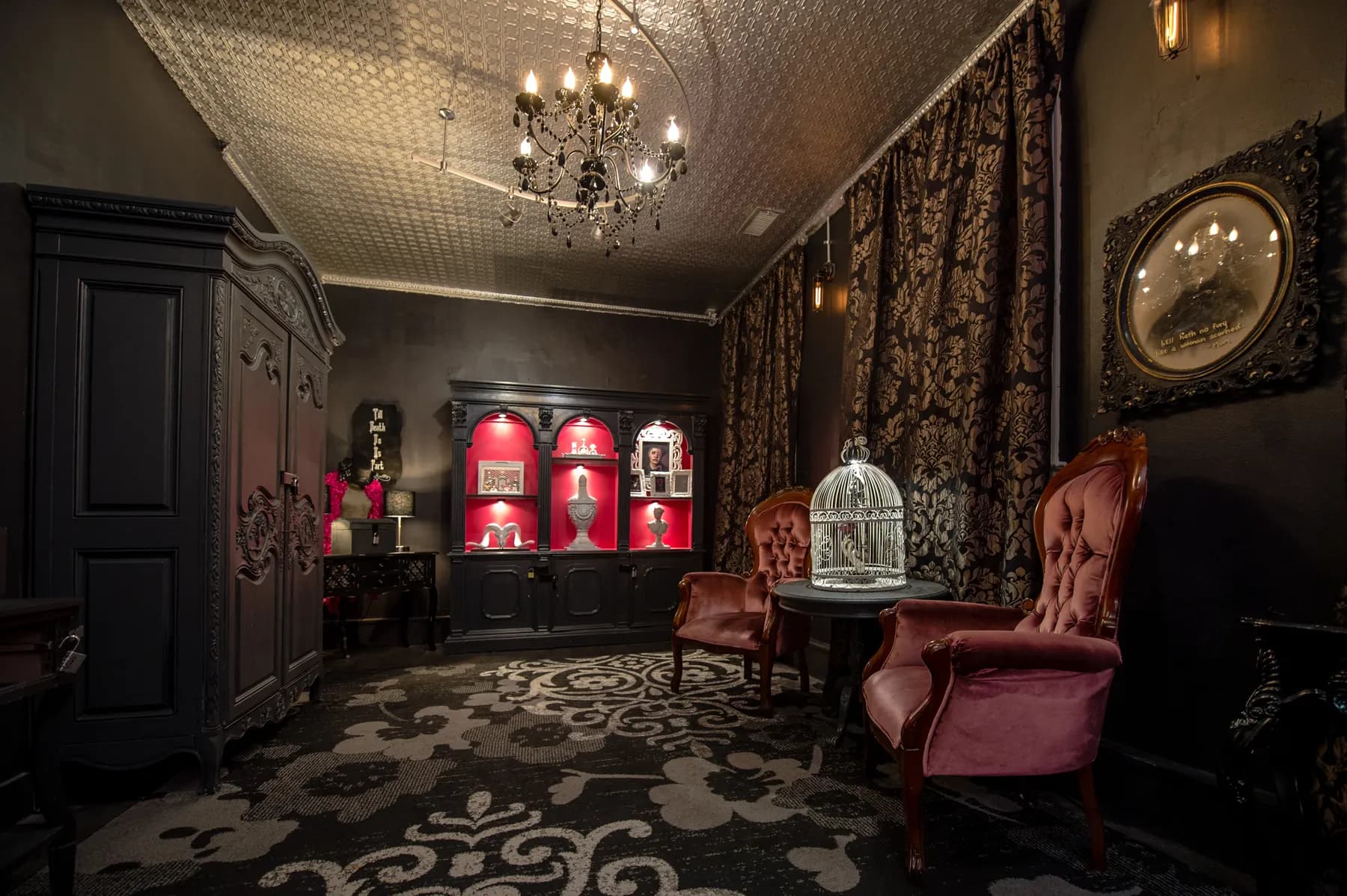 A themed escape room furnished as a Victorian parlour, with a chandelier, red armchairs and a tall wardrobe