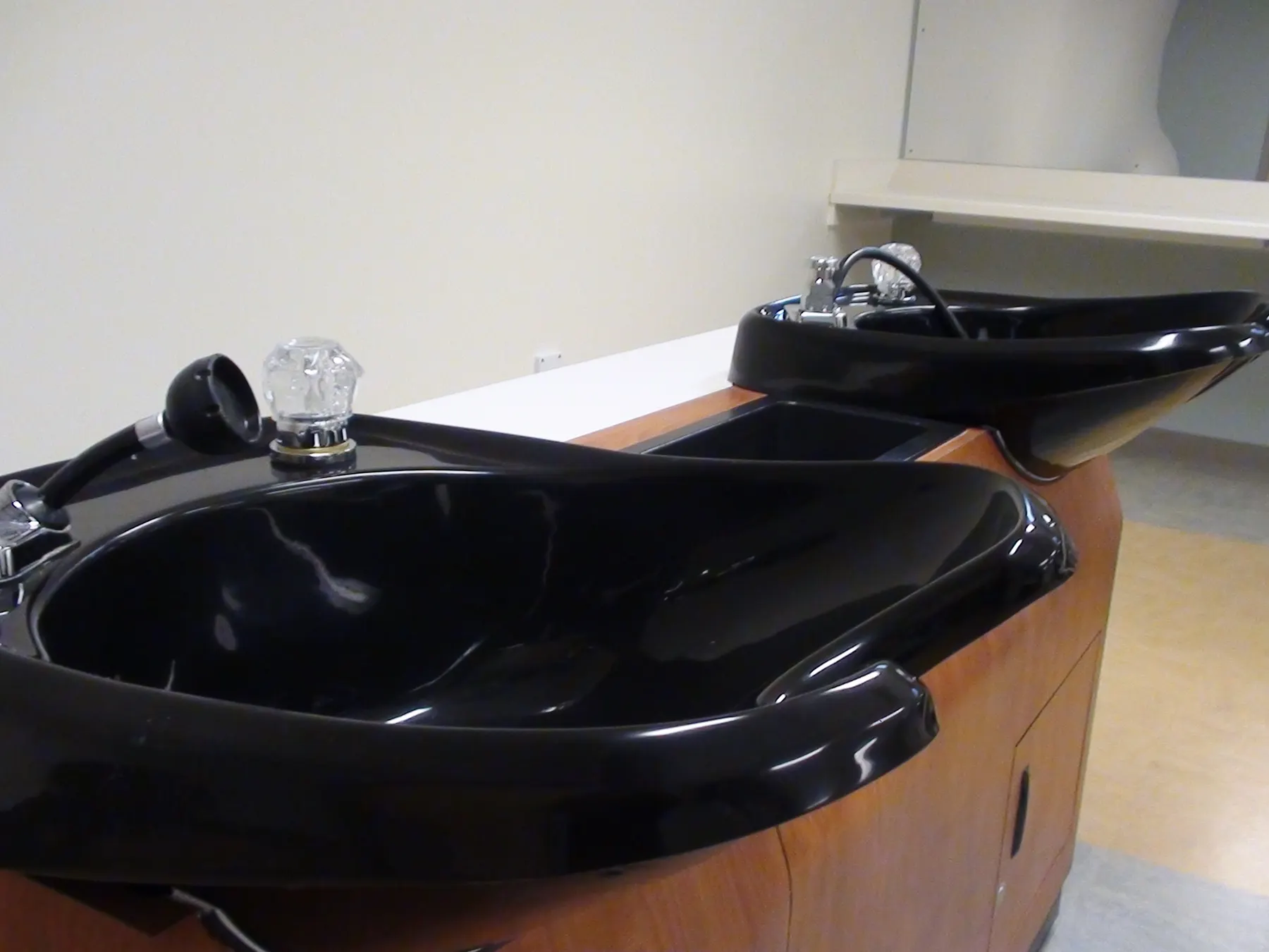 Black hair-washing basins with chrome taps along the wall of a hair salon