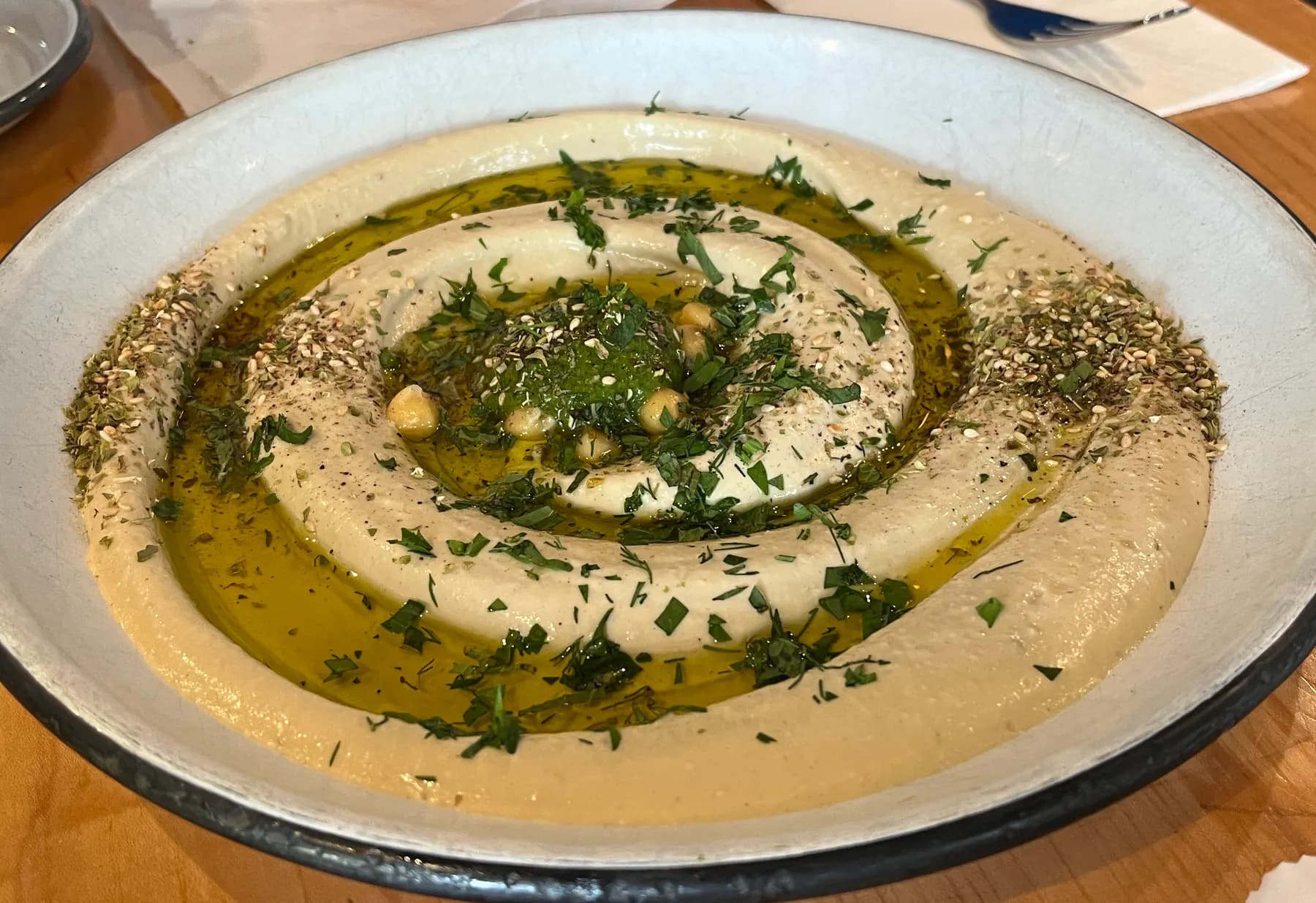A wide plate of hummus with olive oil, za'atar and chopped parsley