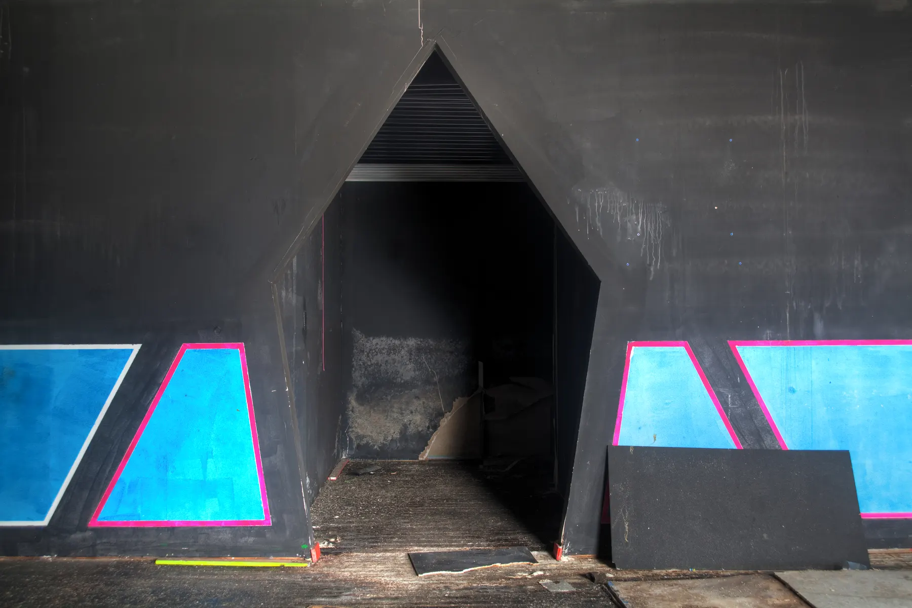 A dark laser tag maze with a pointed doorway and walls painted with glowing blue and pink panels