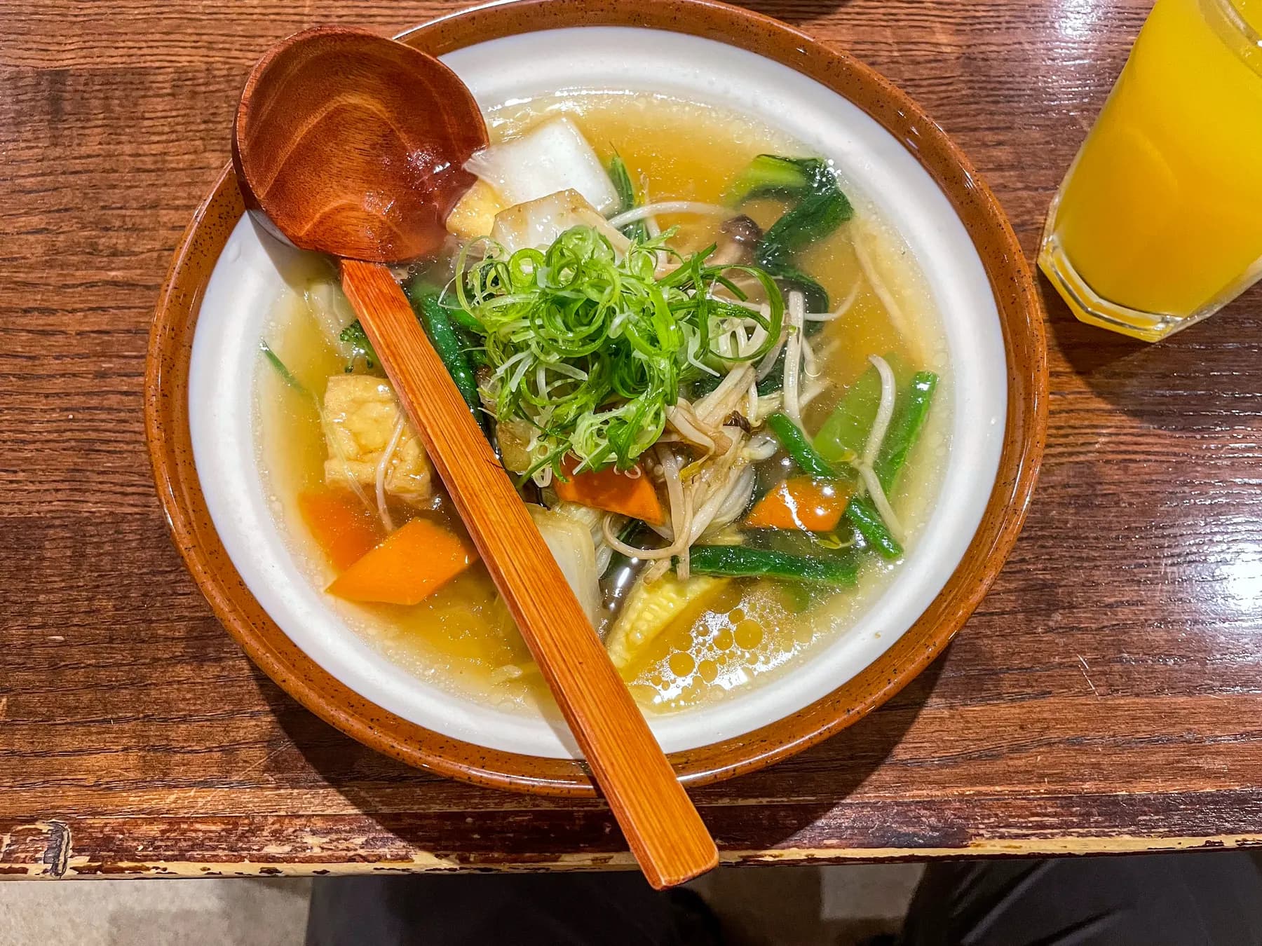A bowl of noodle soup with vegetables, tofu and spring onion, a wooden ladle resting in it