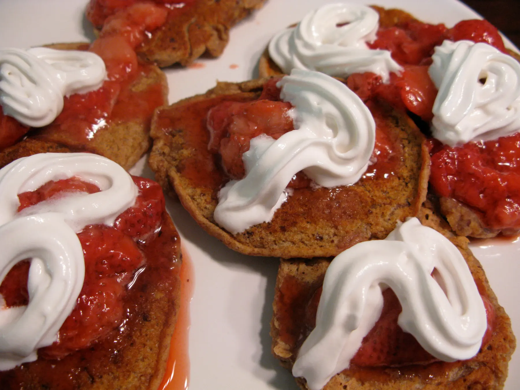 Small vegan pancakes topped with strawberries and swirls of vegan whipped cream