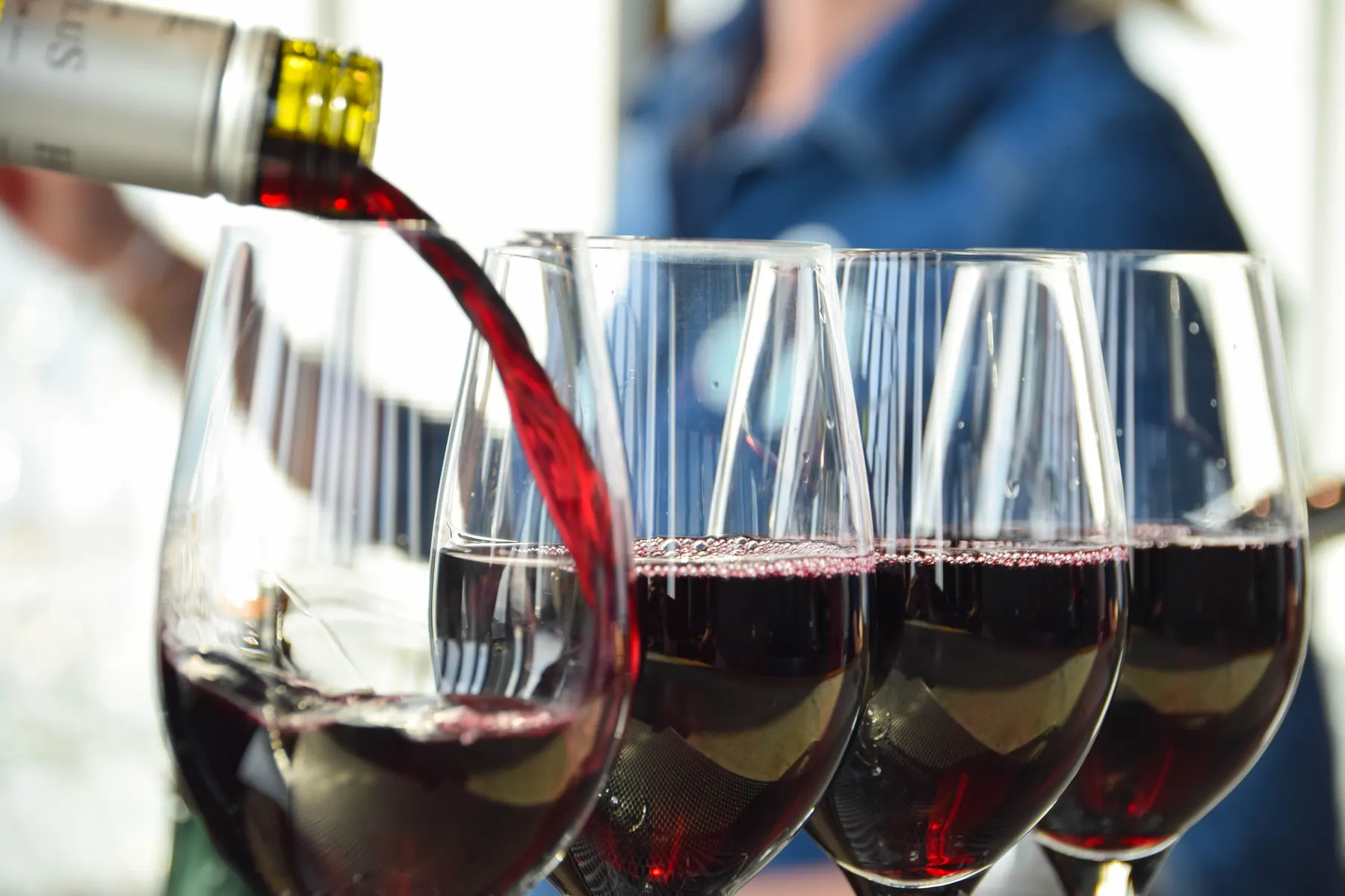 Red wine being poured into a row of glasses at a bar