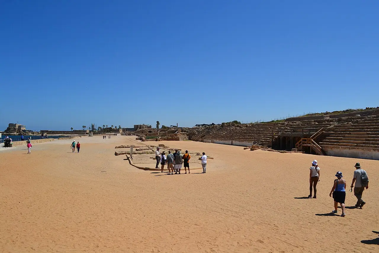 Visitors on the sand floor of Herod's hippodrome at Caesarea, the stone seating to one side