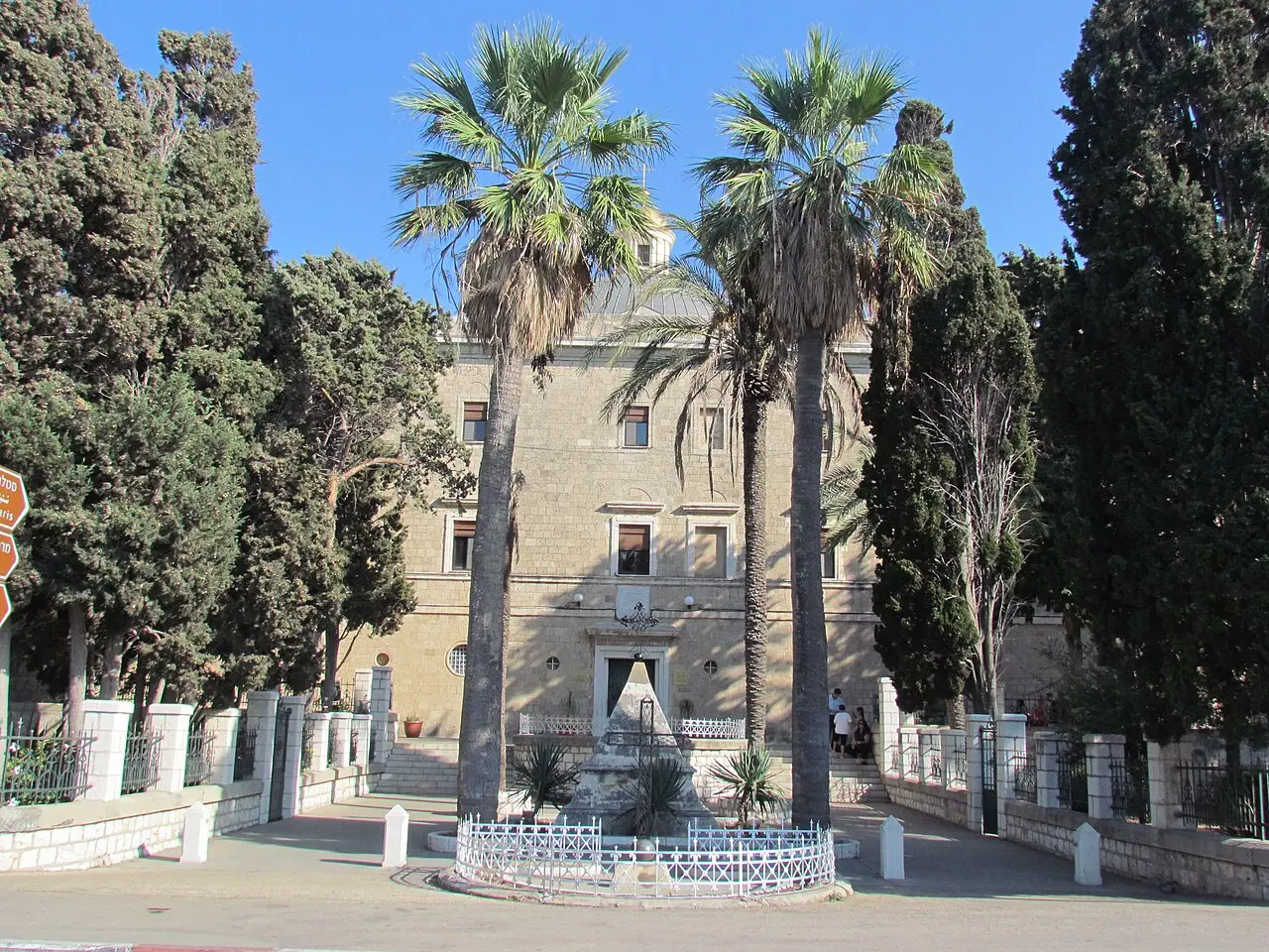 The monastery's front and the statue in its forecourt, between tall palms