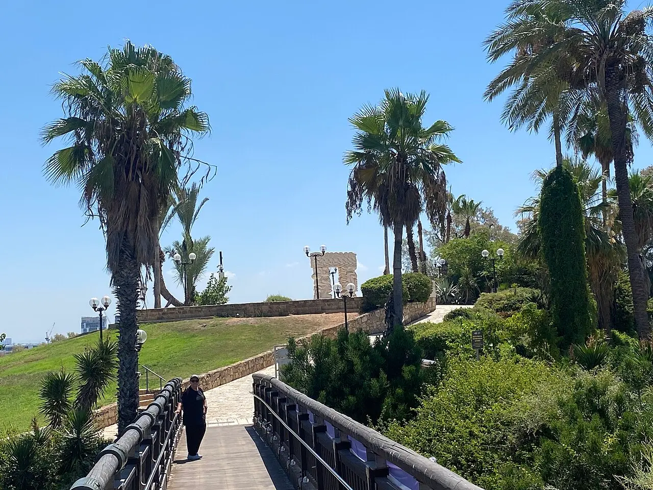 The wooden Wishing Bridge in HaPisga Garden, with the Gate of Faith sculpture on the hill behind