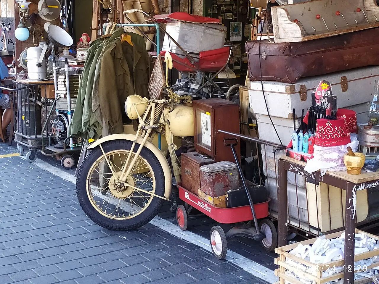 A vintage motorcycle among trunks and bric-a-brac outside a flea-market shop