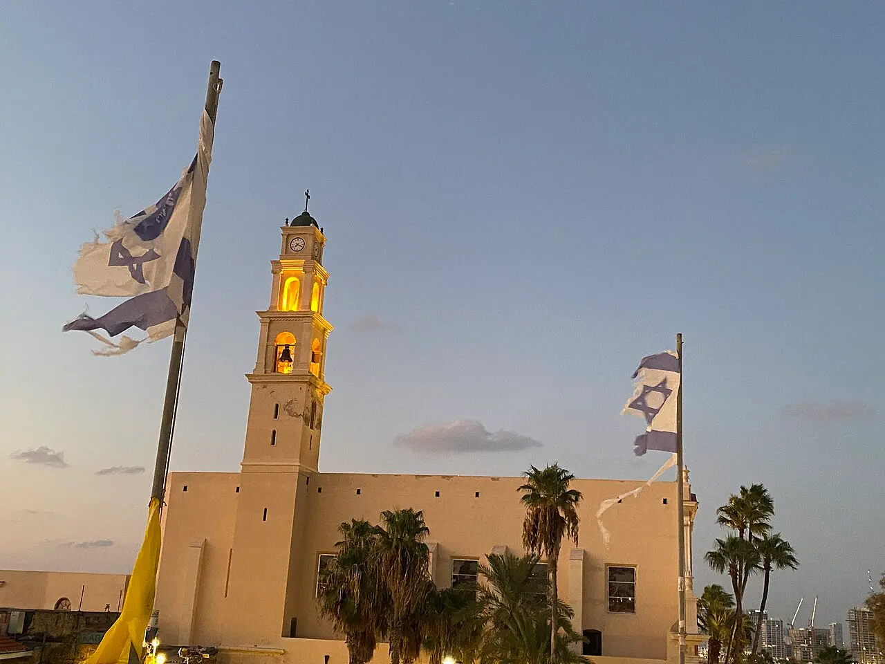 The lit bell tower of St Peter's at dusk, flags flying in the square below