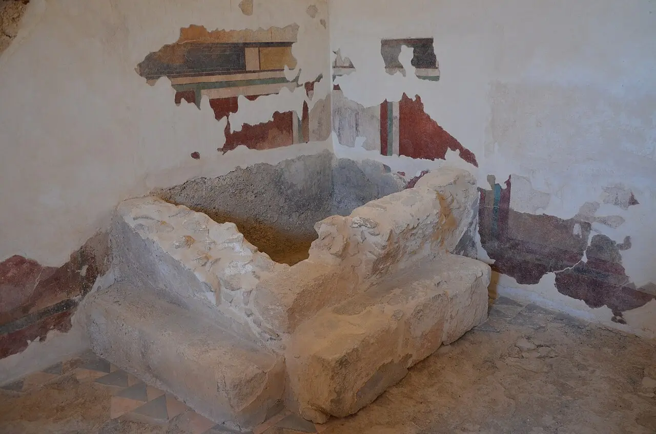 A stone basin in a plastered room of the bathhouse, traces of painted panels on the walls