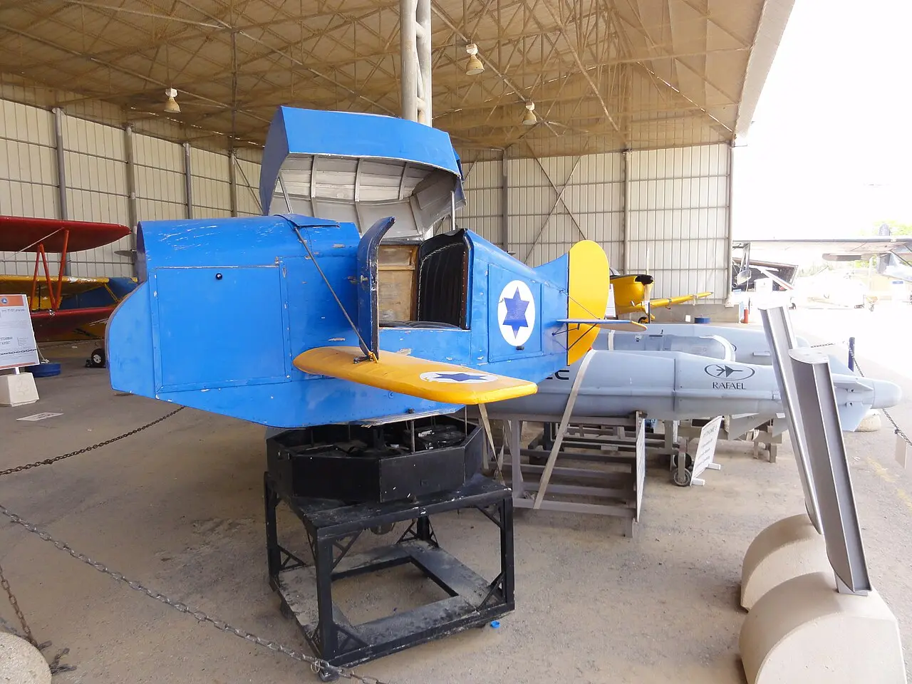 An early aircraft in blue and yellow under the museum's shelter at Hatzerim