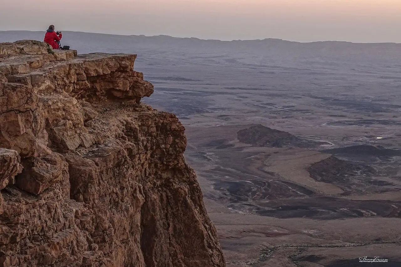 A visitor sitting at the cliff edge above Makhtesh Ramon