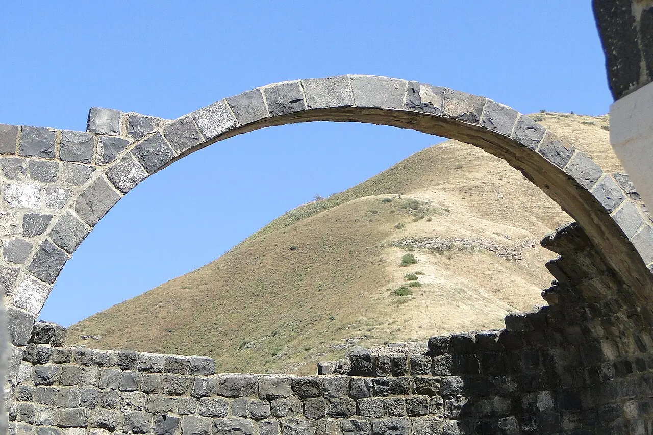 A basalt arch at Kursi framing the hillside above the church