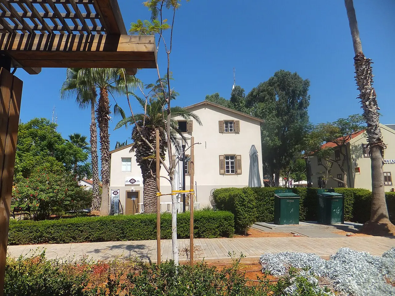 A white Templer house with a red tiled roof in Sarona, a pergola beside it