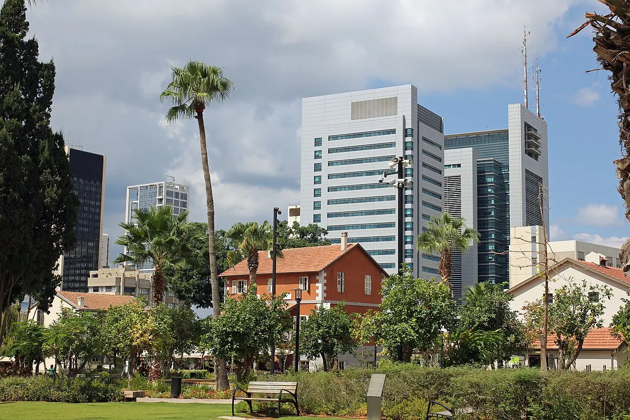 A red-roofed Templer house in Sarona's gardens with office towers rising behind