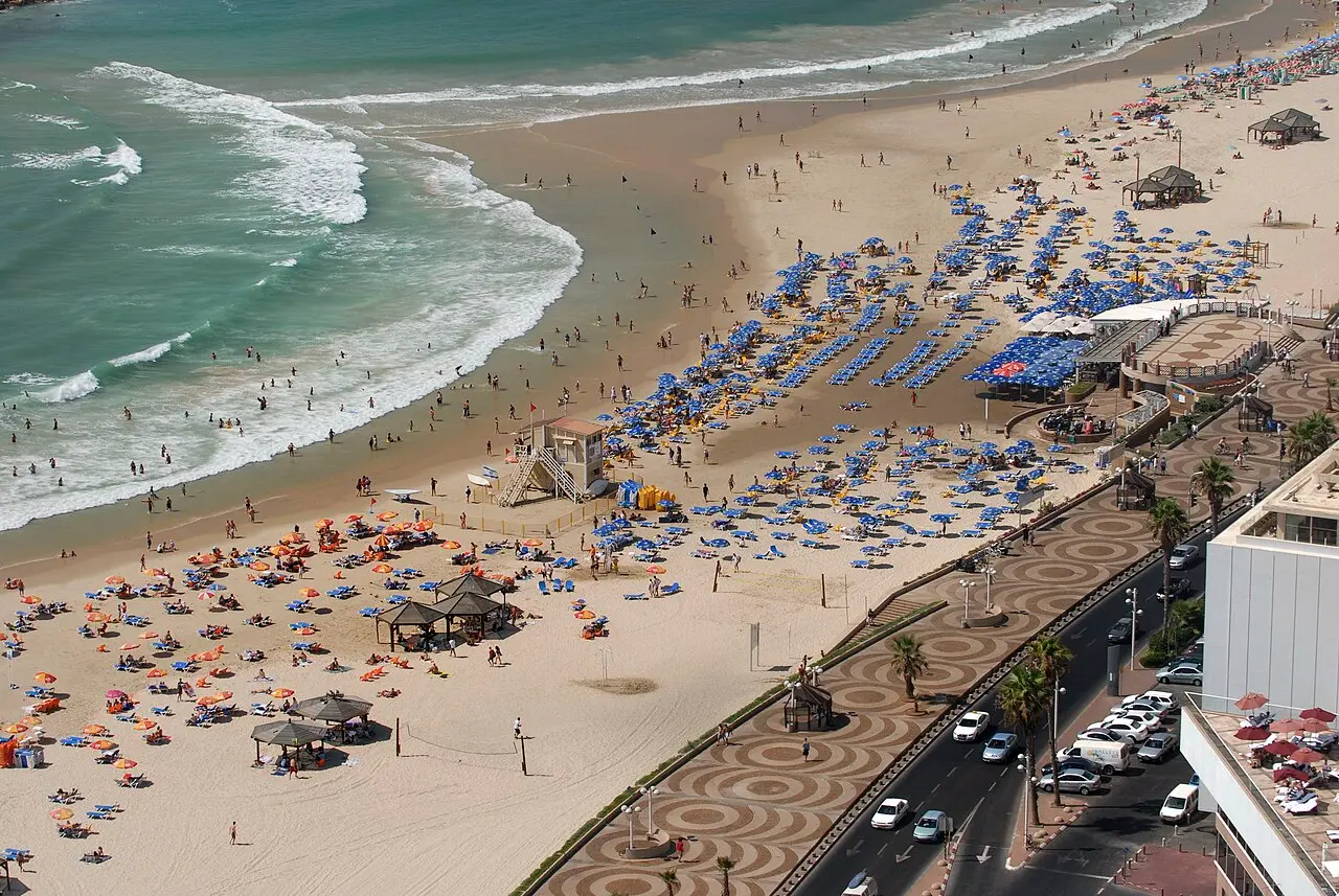 A Tel Aviv beach crowded with umbrellas, the promenade's wave-patterned paving alongside, in 2008